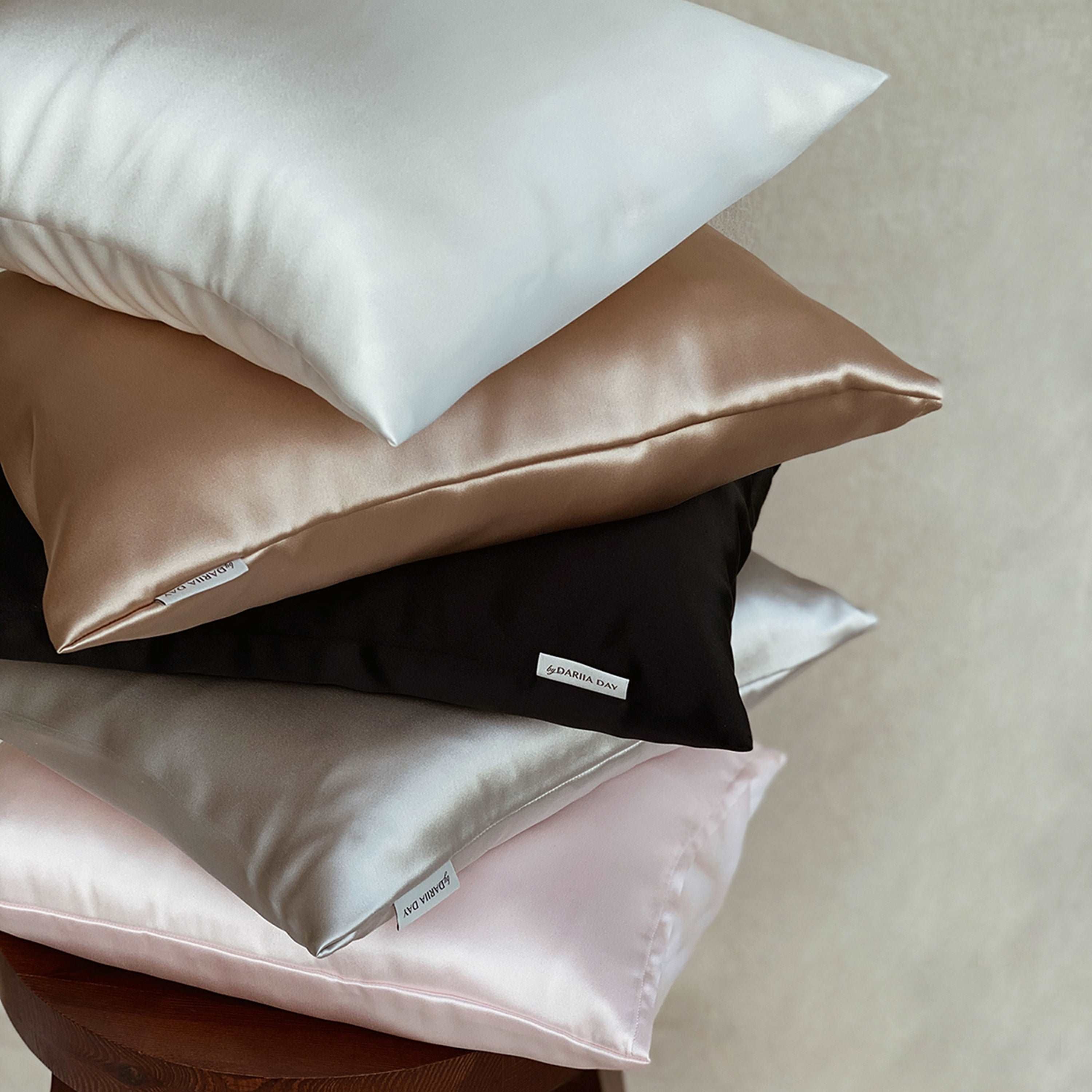 Black Stack of silk pillows in various colors by Dariia Day, including white, beige, black, silver, and blush pink.