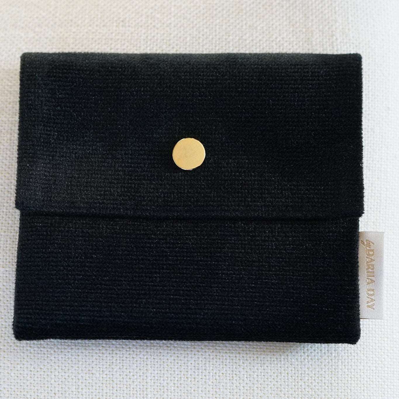 Close-up of the small Dariia Day Midnight Black Velvet Pouch on a beige surface.