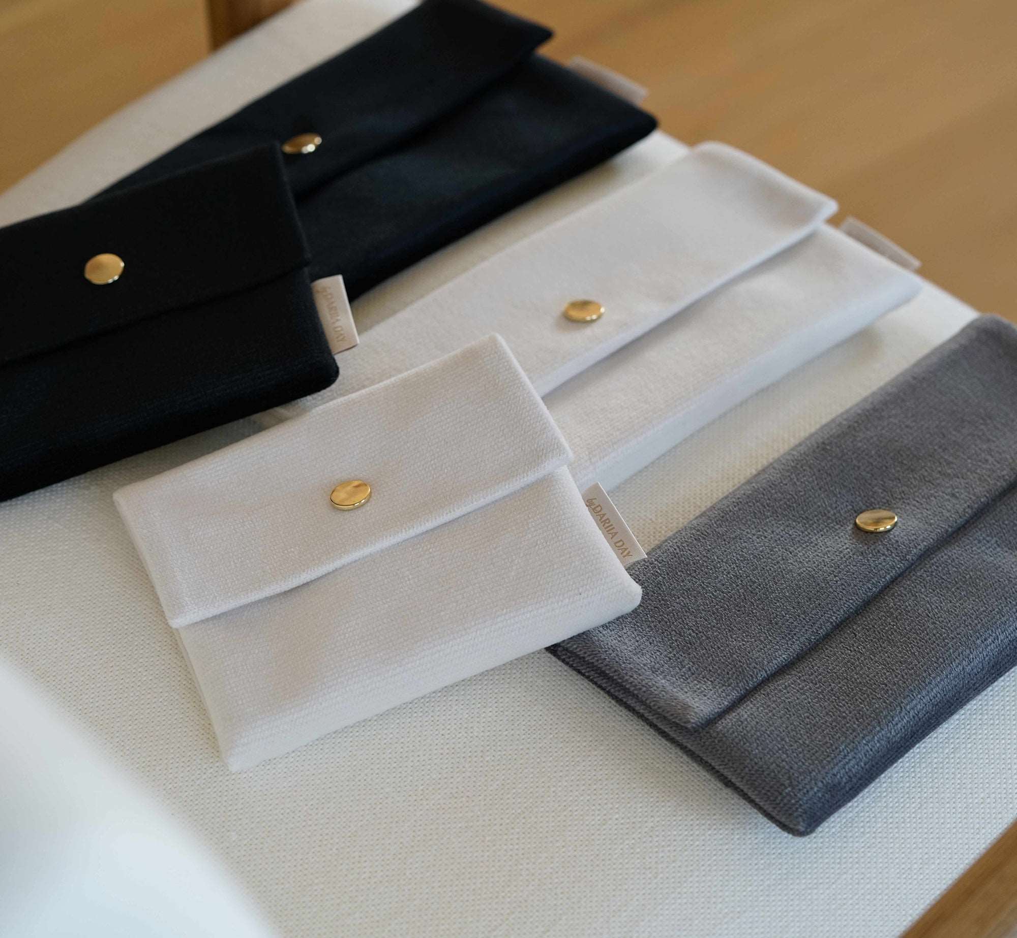 Multiple velvet pouches in Midnight Black, Powder White, and Silver Grey from Dariia Day, elegantly arranged.