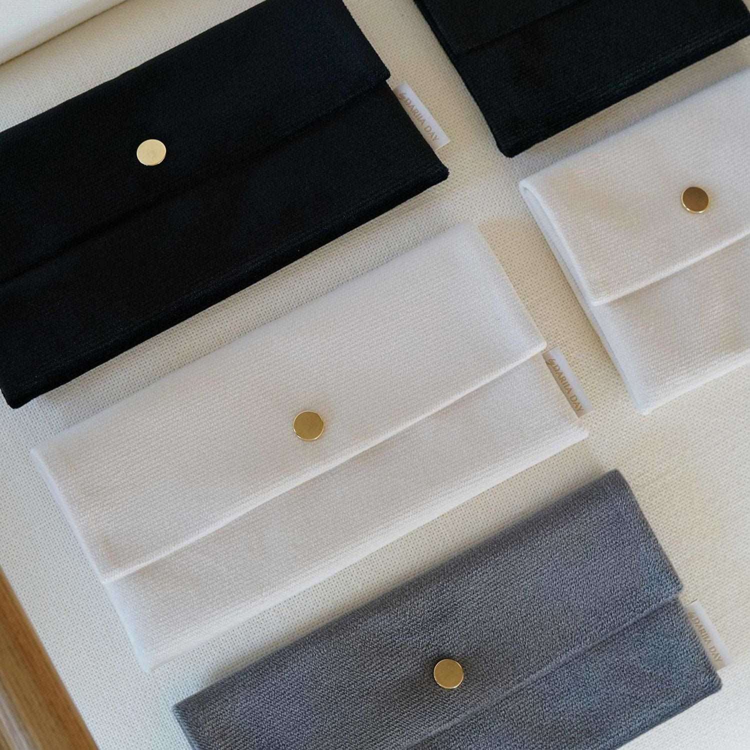 Dariia Day Velvet Pouch collection in Midnight Black, Powder White, and Silver Grey displayed on a beige surface.