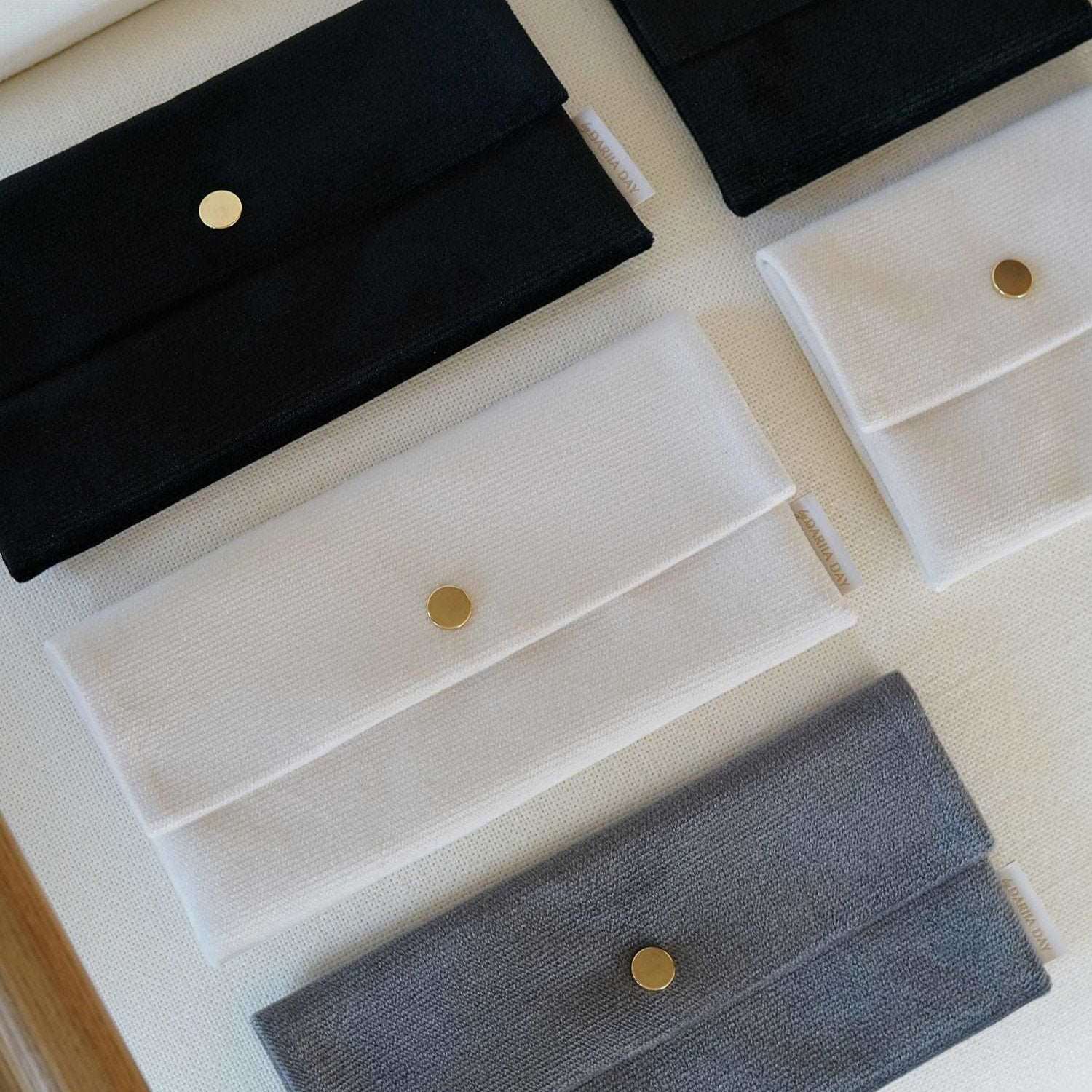 Dariia Day Velvet Pouch collection in Midnight Black, Powder White, and Silver Grey displayed on a beige surface.