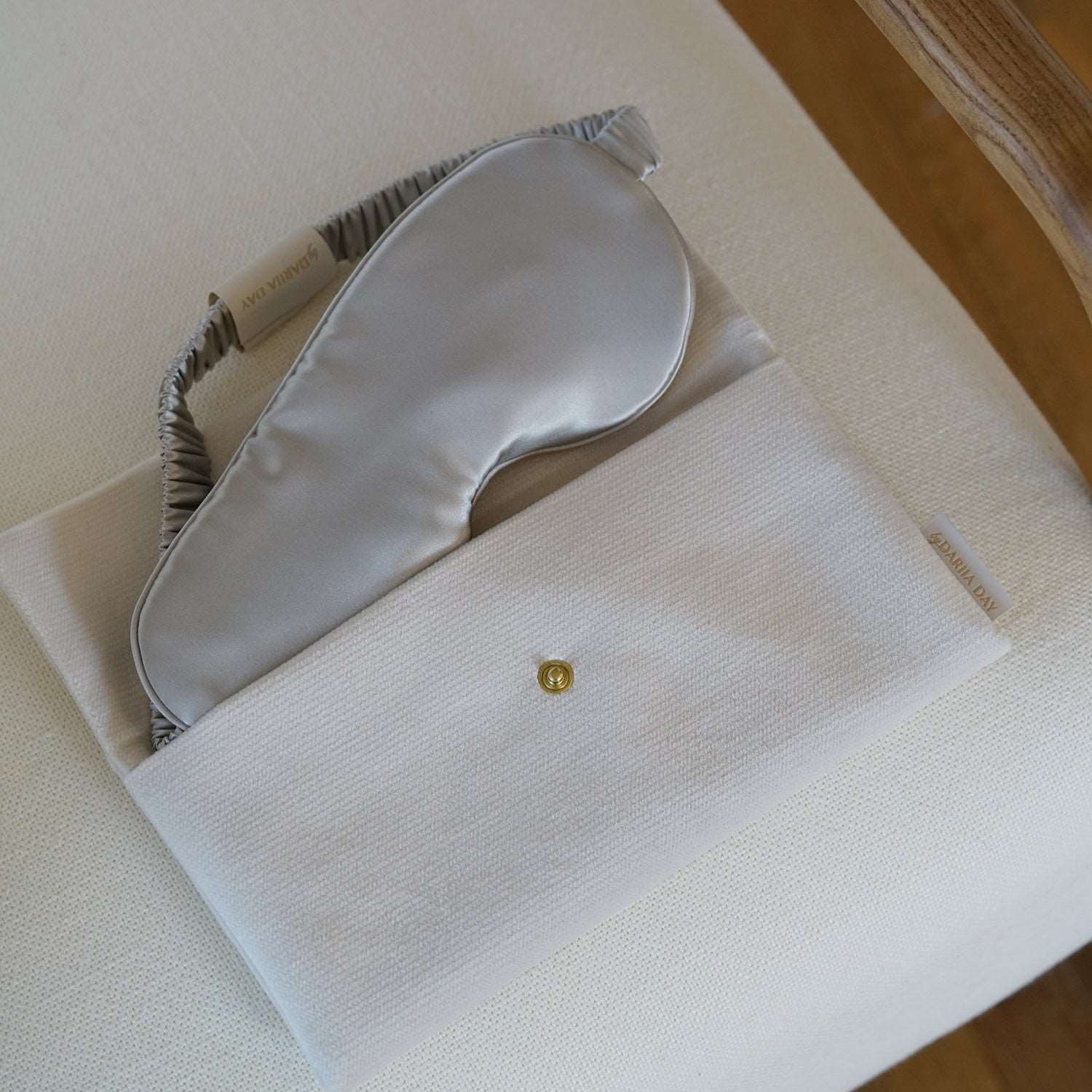 Dariia Day White Vanilla Pouch holding a silk eye mask, displayed on a beige chair.