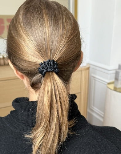 Back view of a woman with blonde hair tied in a ponytail using a Dariia Day XS silk scrunchie in Midnight Black.