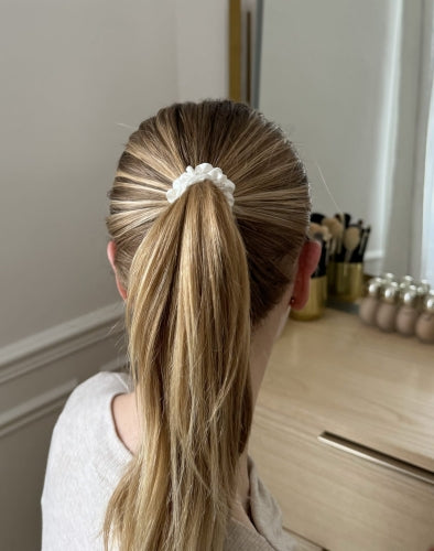 Back view of a woman with blonde hair styled in a ponytail using a Dariia Day XS silk scrunchie in Powder White.