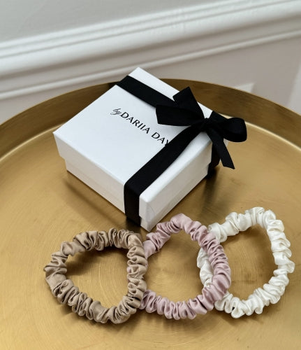 Variety of XS silk scrunchies by Dariia Day, including Pink Blush, Beige and Powder White laid on a gold tray with product tags.