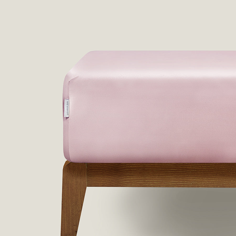 Luxury blush pink fitted silk sheet made from 100% mulberry silk on a bed.