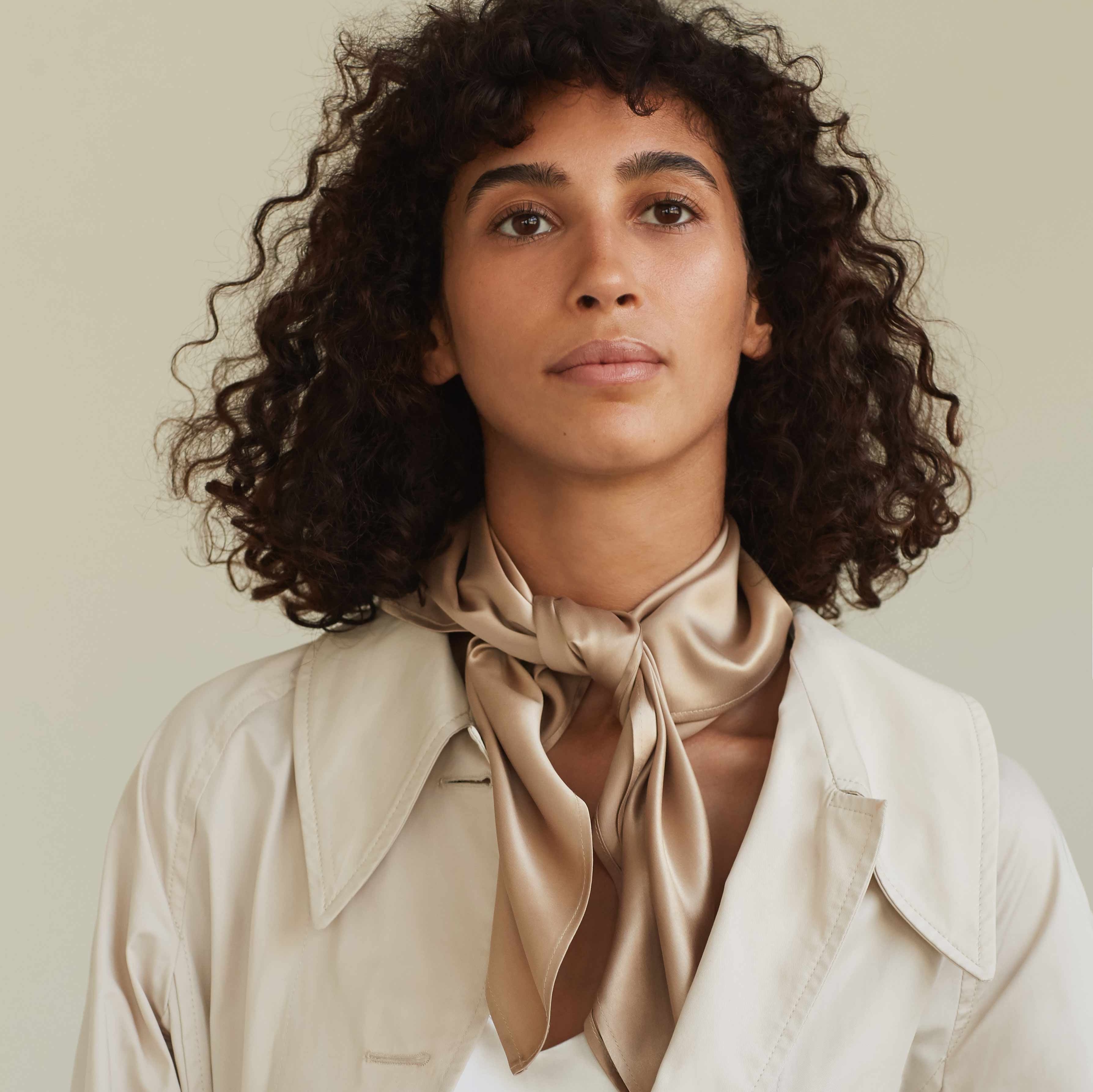 A hand holding a luxurious French beige silk scarf by Dariia Day, showcasing its smooth and soft fabric