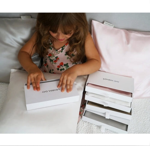 Young girl unboxing a set of silk pillowcases by Dariia Day, with luxurious soft pillowcases displayed around her.