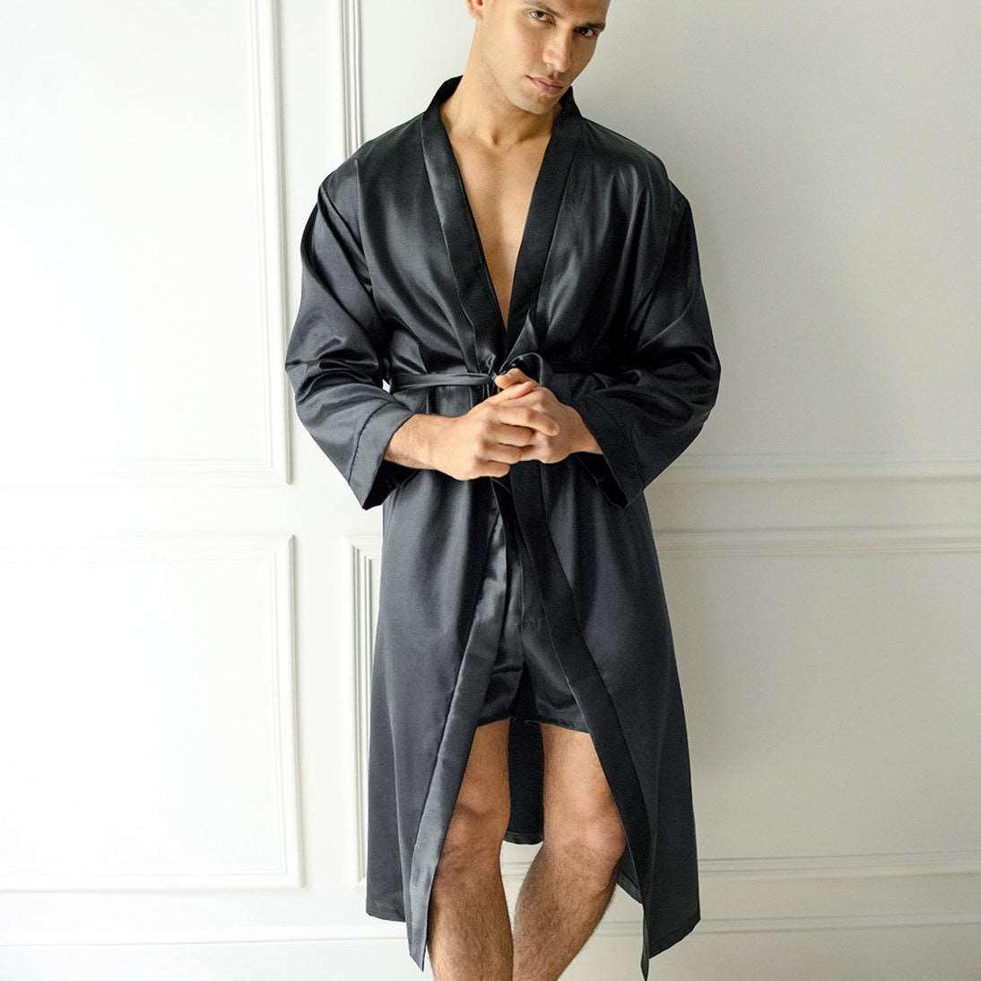 Man wearing a black silk robe with matching shorts by Dariia Day, standing against a wall.