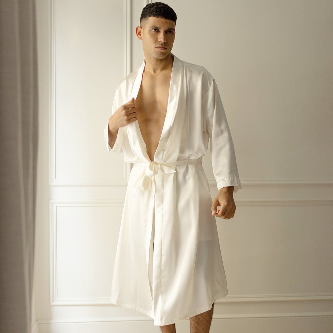 Man wearing a powder white silk robe by Dariia Day, standing in a minimalistic room with natural light.
