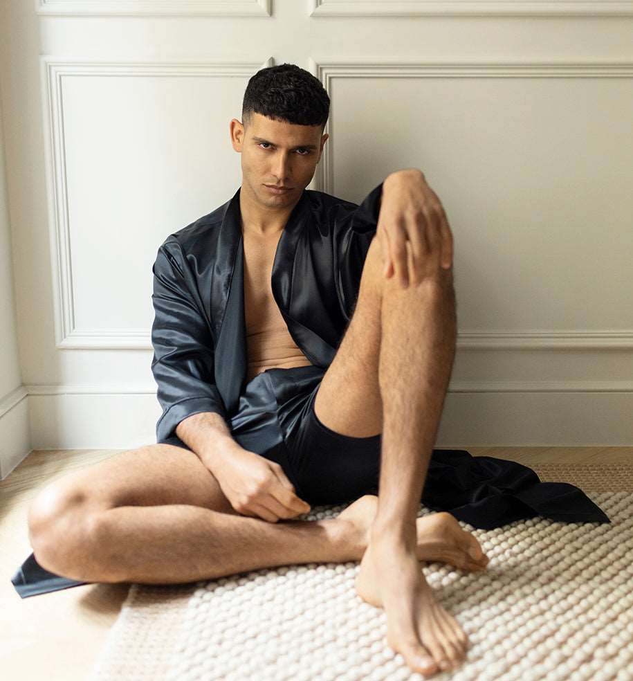 Black Man sitting on the floor wearing black silk boxers and a matching silk robe by Dariia Day, highlighting the luxurious fabric.