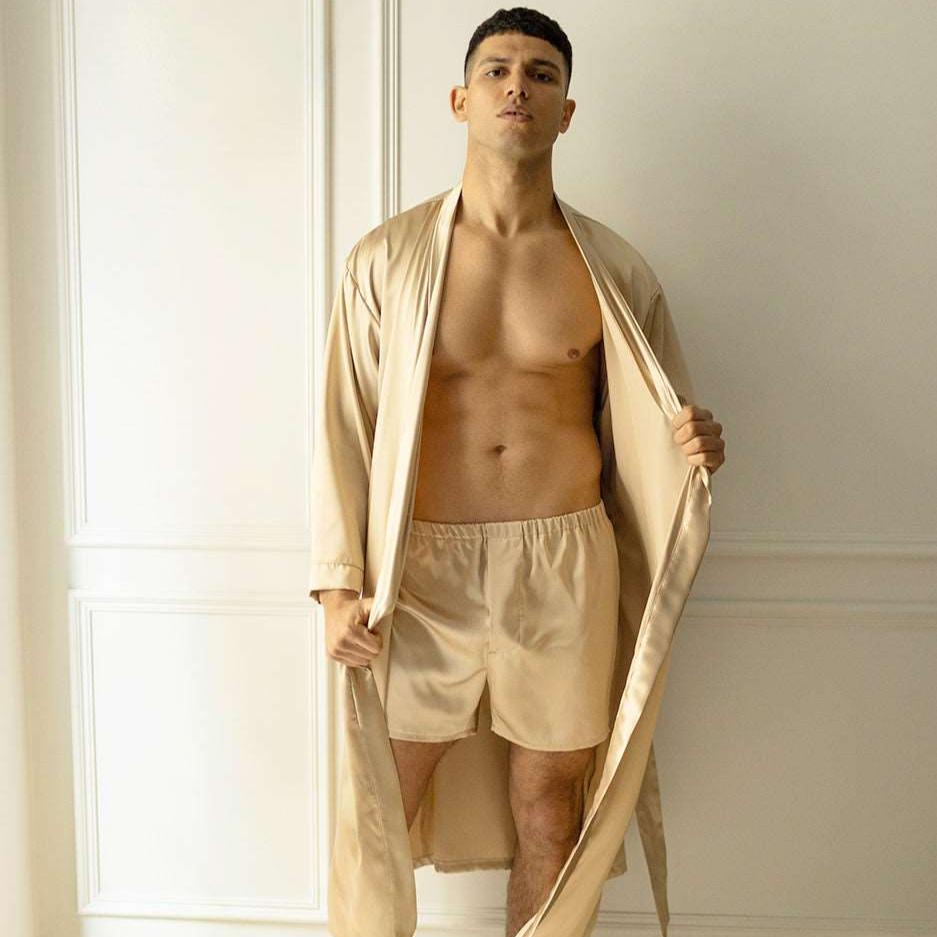 Beige Man posing in French beige silk boxers and a robe by Dariia Day, standing in a modern room.