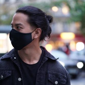 Man wearing a midnight black silk face mask styled with a black denim jacket, street style during the evening.