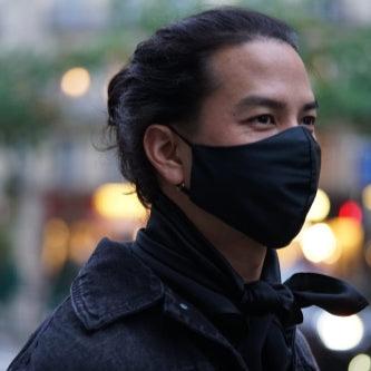 Man wearing a midnight black silk face mask paired with a denim jacket and a scarf, evening street style.