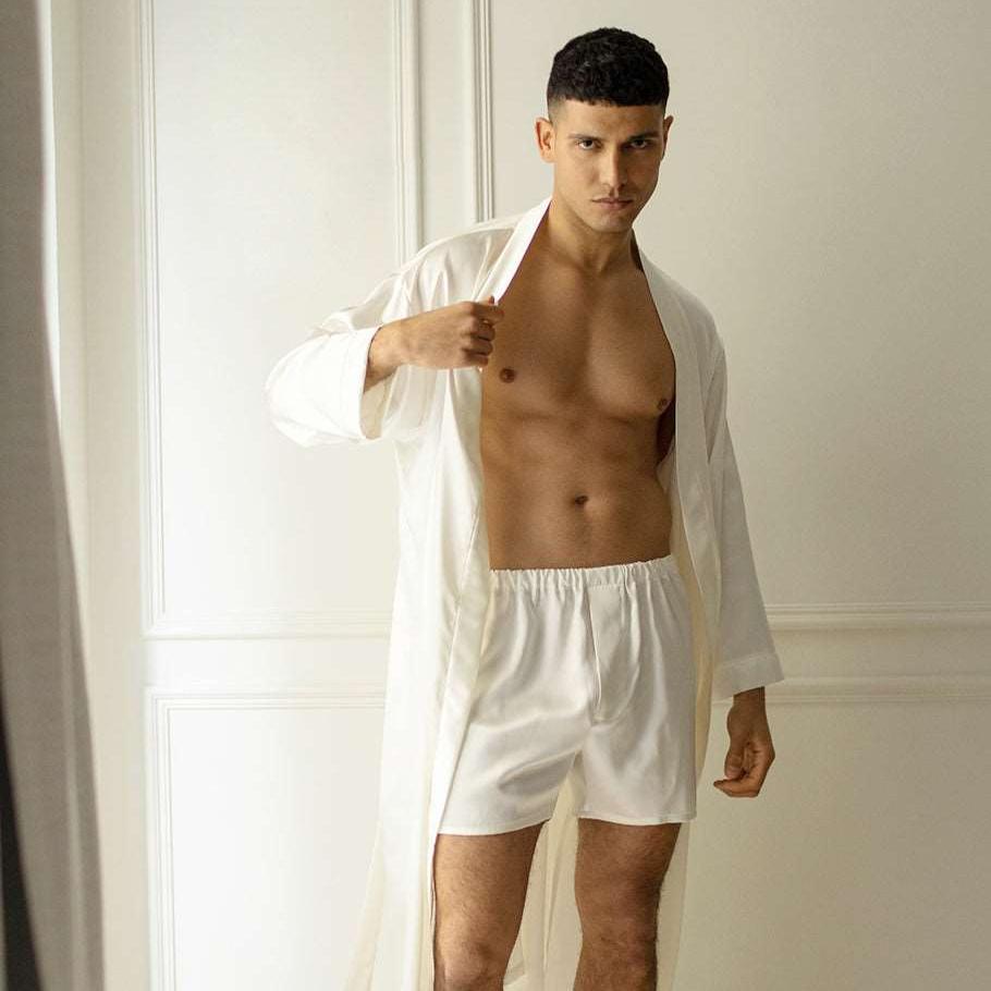 White Man wearing white silk boxers and a matching robe by Dariia Day, standing in a modern bedroom.