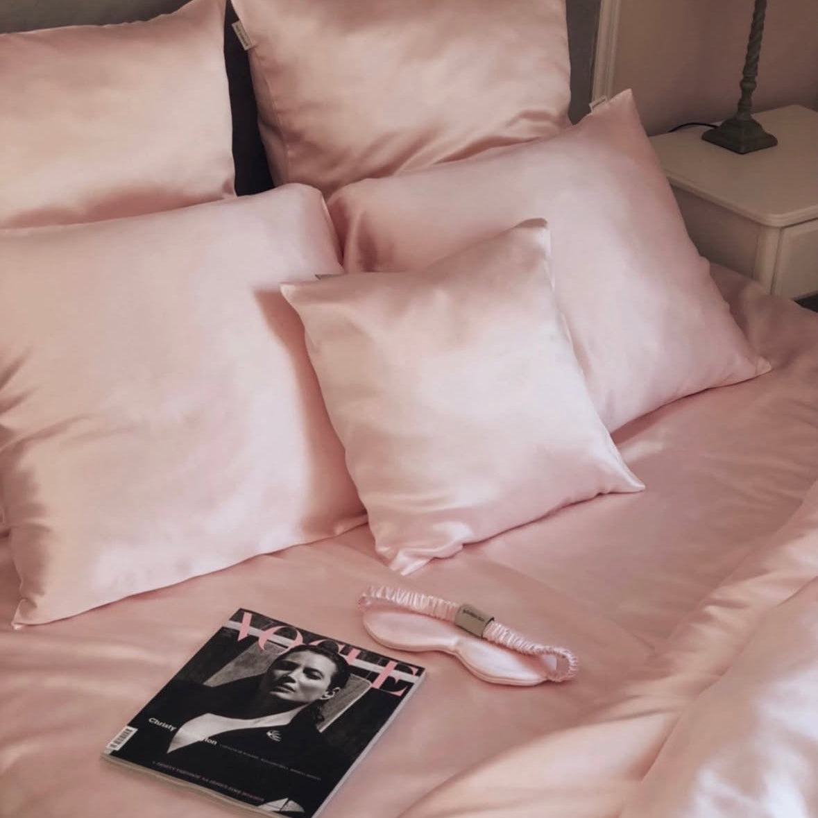 Pink Bedroom setup featuring a pink blush silk duvet cover and pillow set by Dariia Day, with a magazine and silk eye mask placed on the bed, highlighting the elegant and cozy aesthetic.