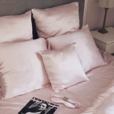 Bedroom setup featuring a pink blush silk duvet cover and pillow set by Dariia Day, with a magazine and silk eye mask placed on the bed, highlighting the elegant and cozy aesthetic.