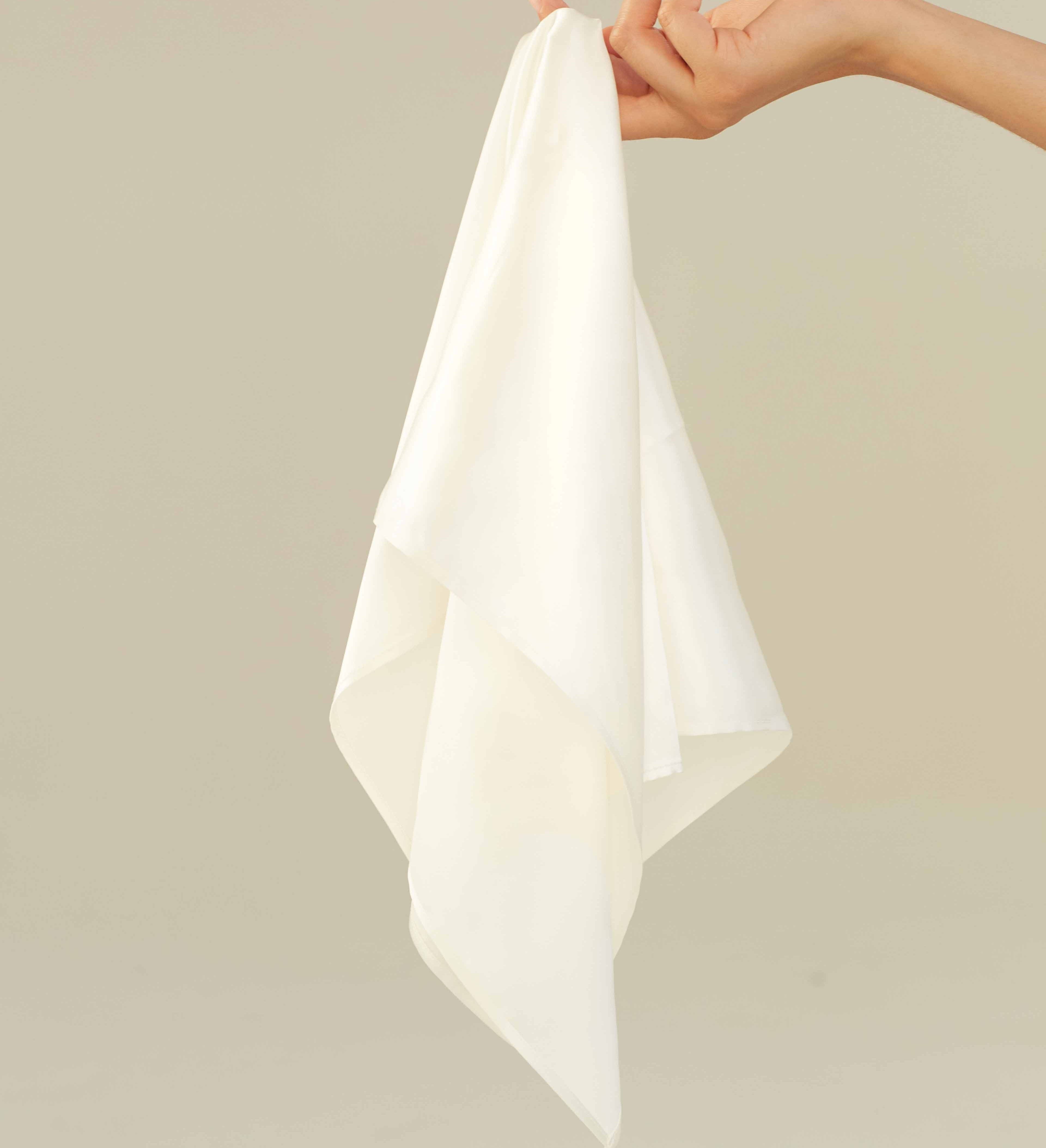 A hand holding a powder white silk scarf by Dariia Day, showcasing its soft and luxurious fabric