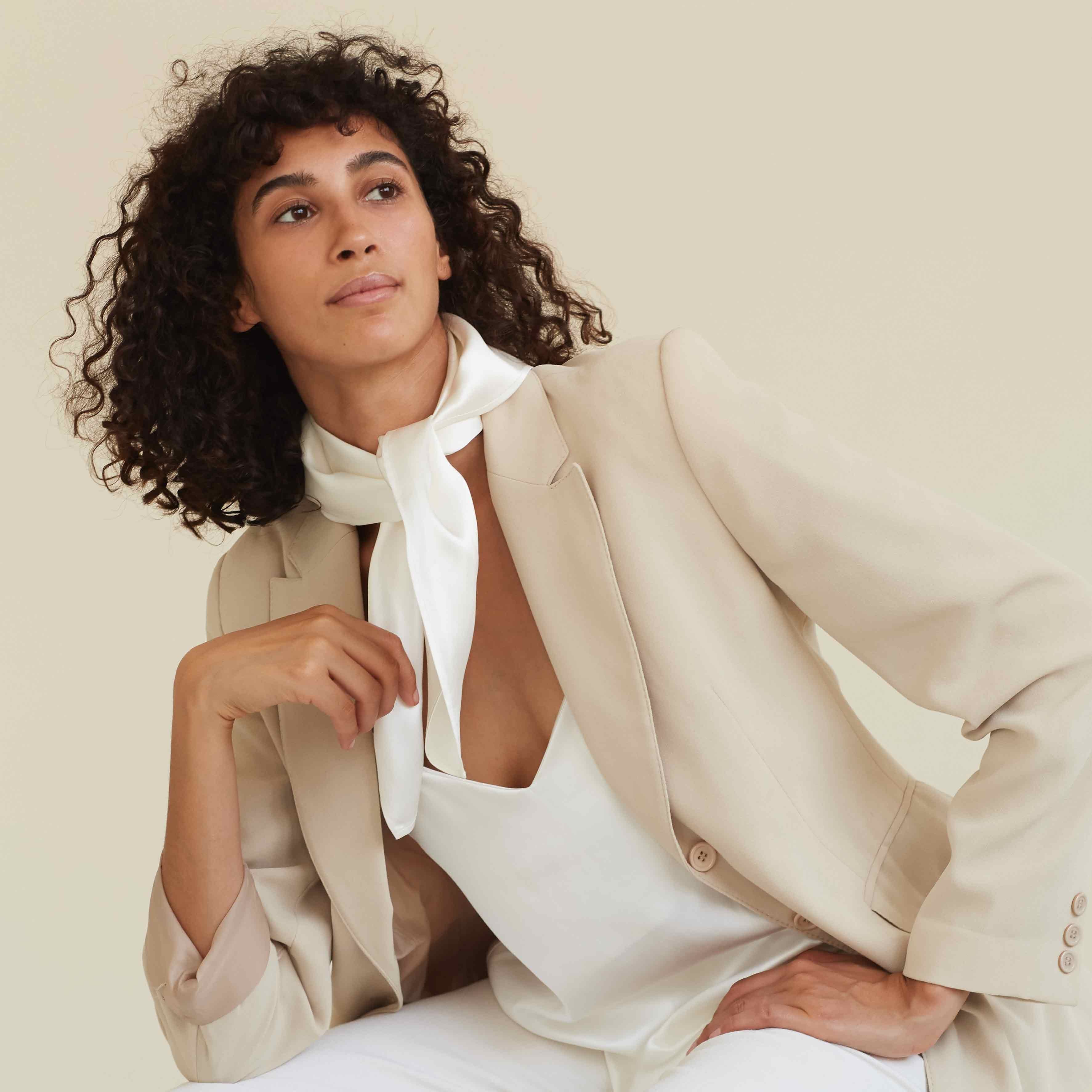 A woman wearing a powder white silk scarf by Dariia Day, tied elegantly around her neck, minimal and sophisticated style