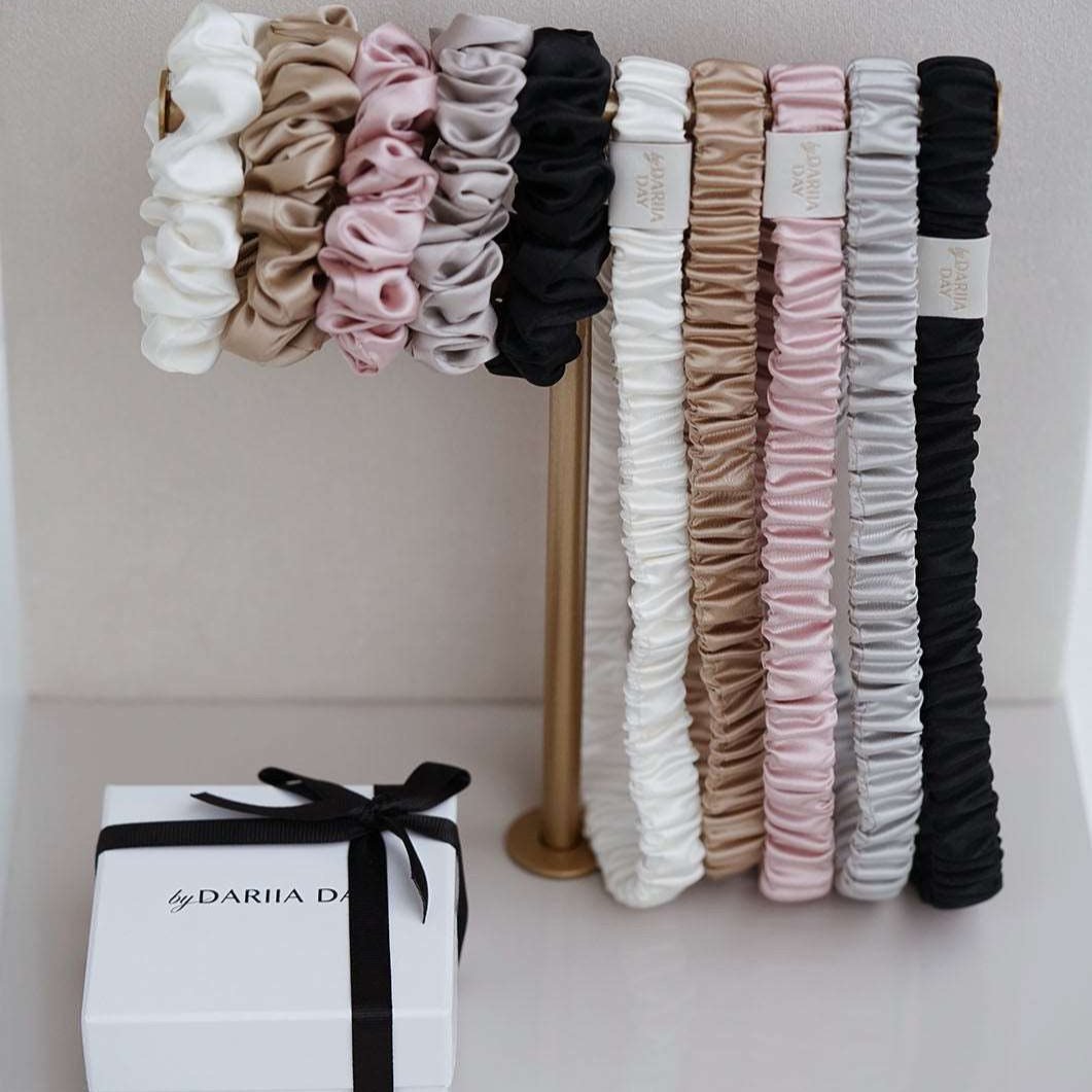 Silk scrunchies and headbands collection by Dariia Day in various colors displayed on a stand.