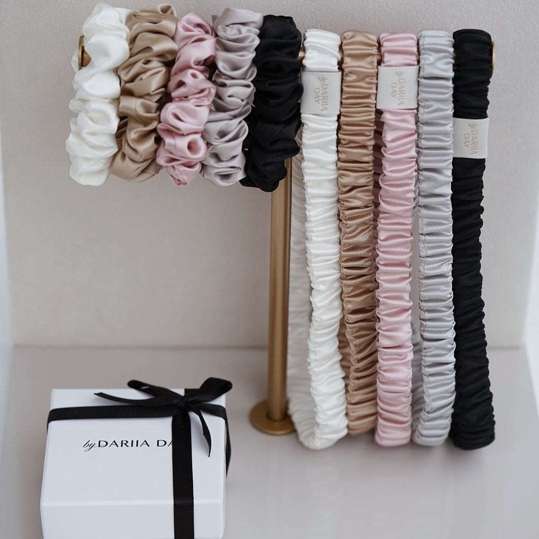 Silk scrunchies and headbands collection by Dariia Day in various colors displayed on a stand.