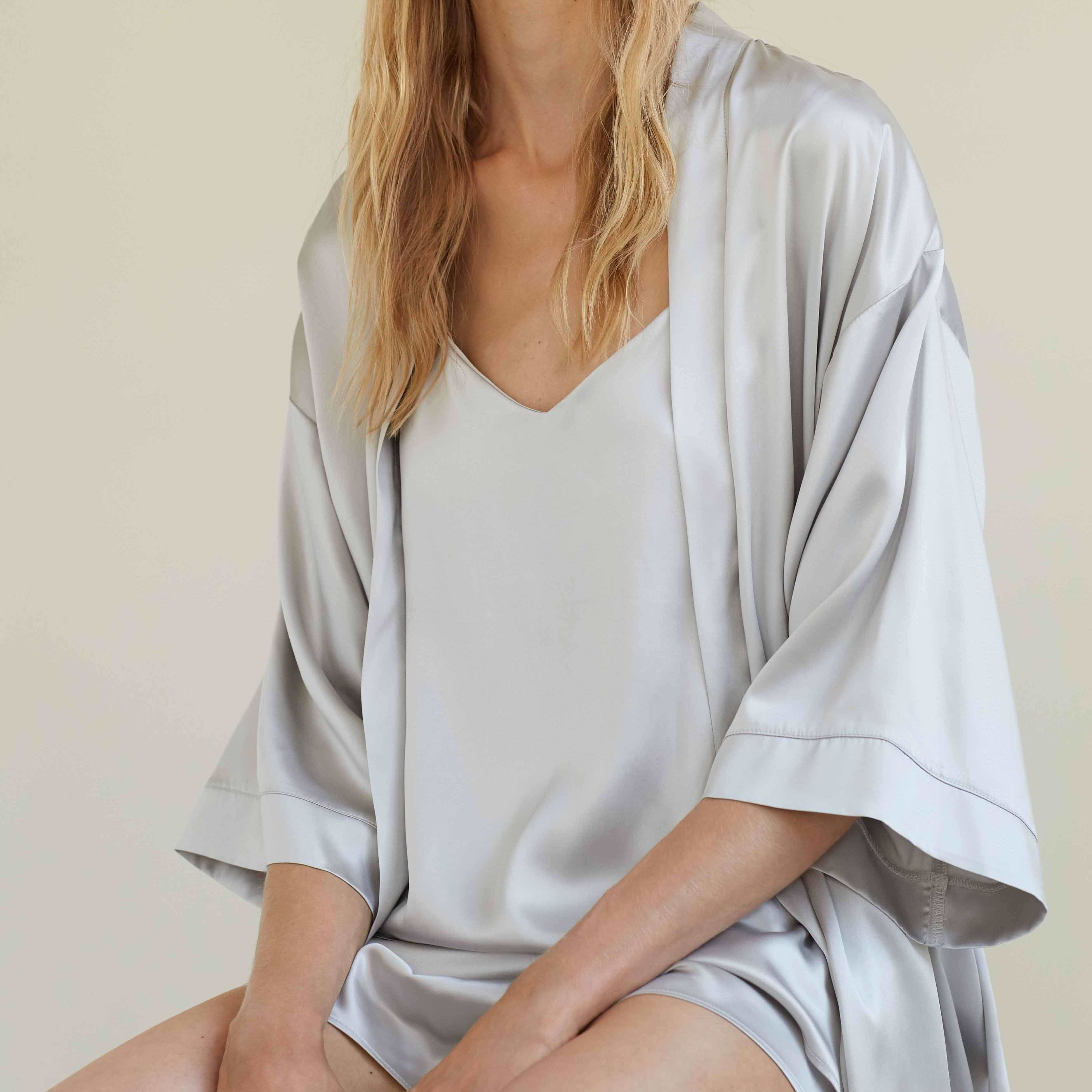 Woman sitting in a silver grey silk robe and camisole set by Dariia Day, enjoying the soft and luxurious fabric.