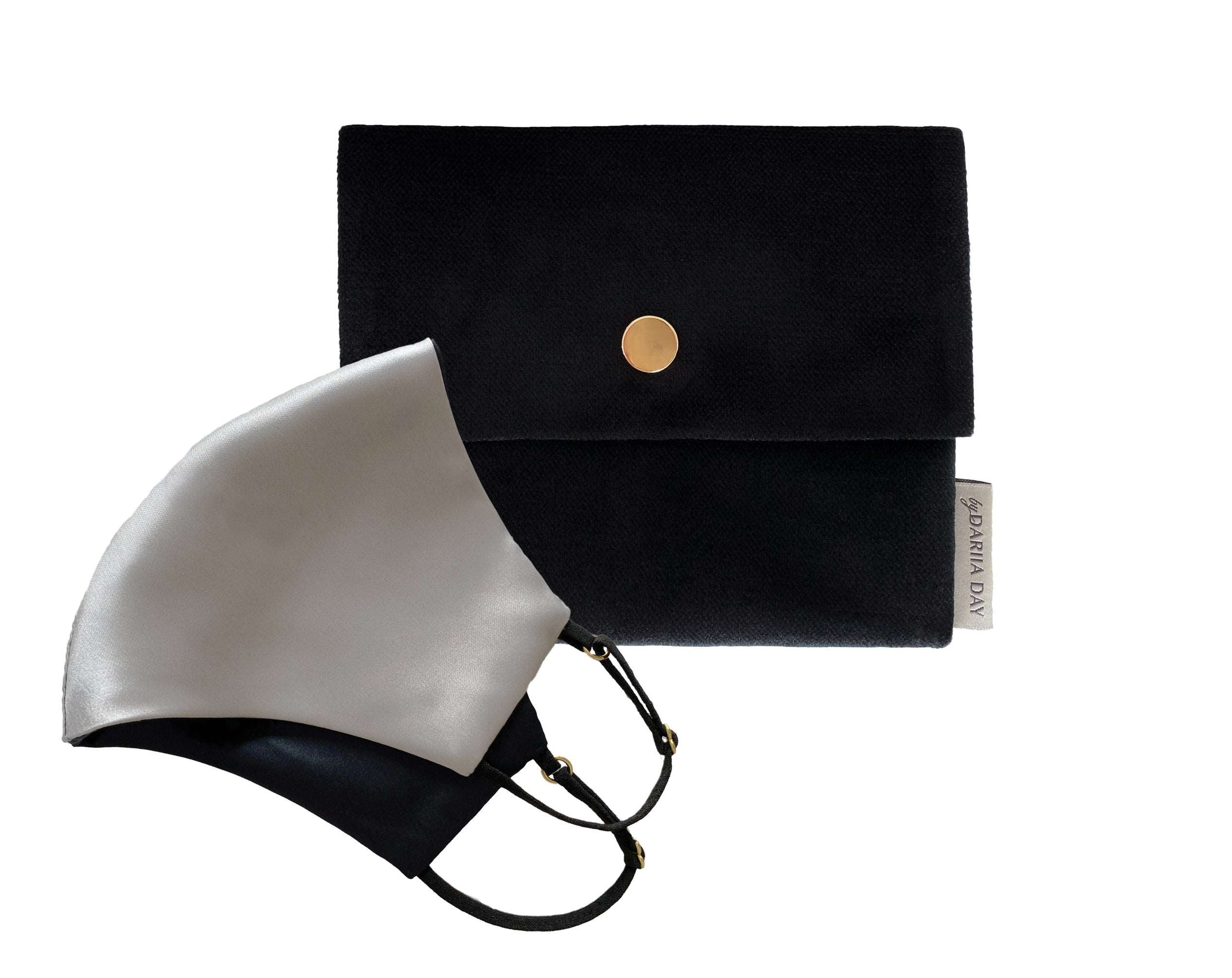 Silver grey silk face mask with black straps, displayed next to a black pouch with a gold button closure.