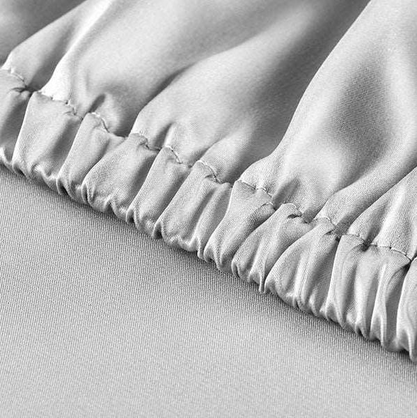 Detailed close-up of the elastic edge on a silver grey silk fitted sheet, displaying the premium craftsmanship and snug fit.