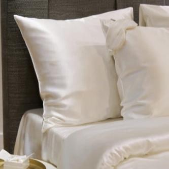 White silk duvet and pillows by Dariia Day, arranged on a bed with a grey headboard and a round bedside table, showcasing the soft and glossy silk texture.