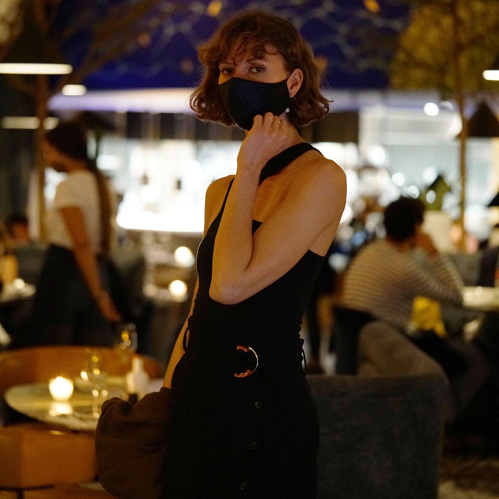 Woman wearing a midnight black silk face mask by Dariia Day in an elegant restaurant.