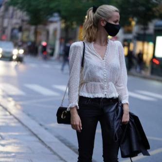 Fashionable woman in a white blouse and black leather pants wearing a midnight black silk face mask while standing on a city street.